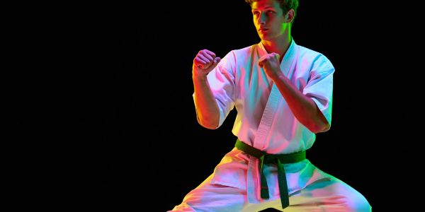 Martial artist in a karate stance with colorful lighting on black background.