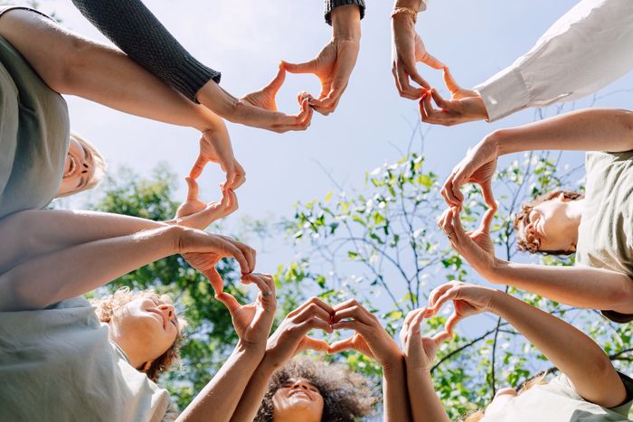 Group of people forming heart shapes with their hands under the sky.