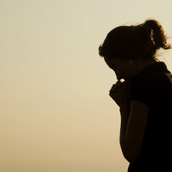 Silhouette of a woman deep in thought against a soft sunset sky.
