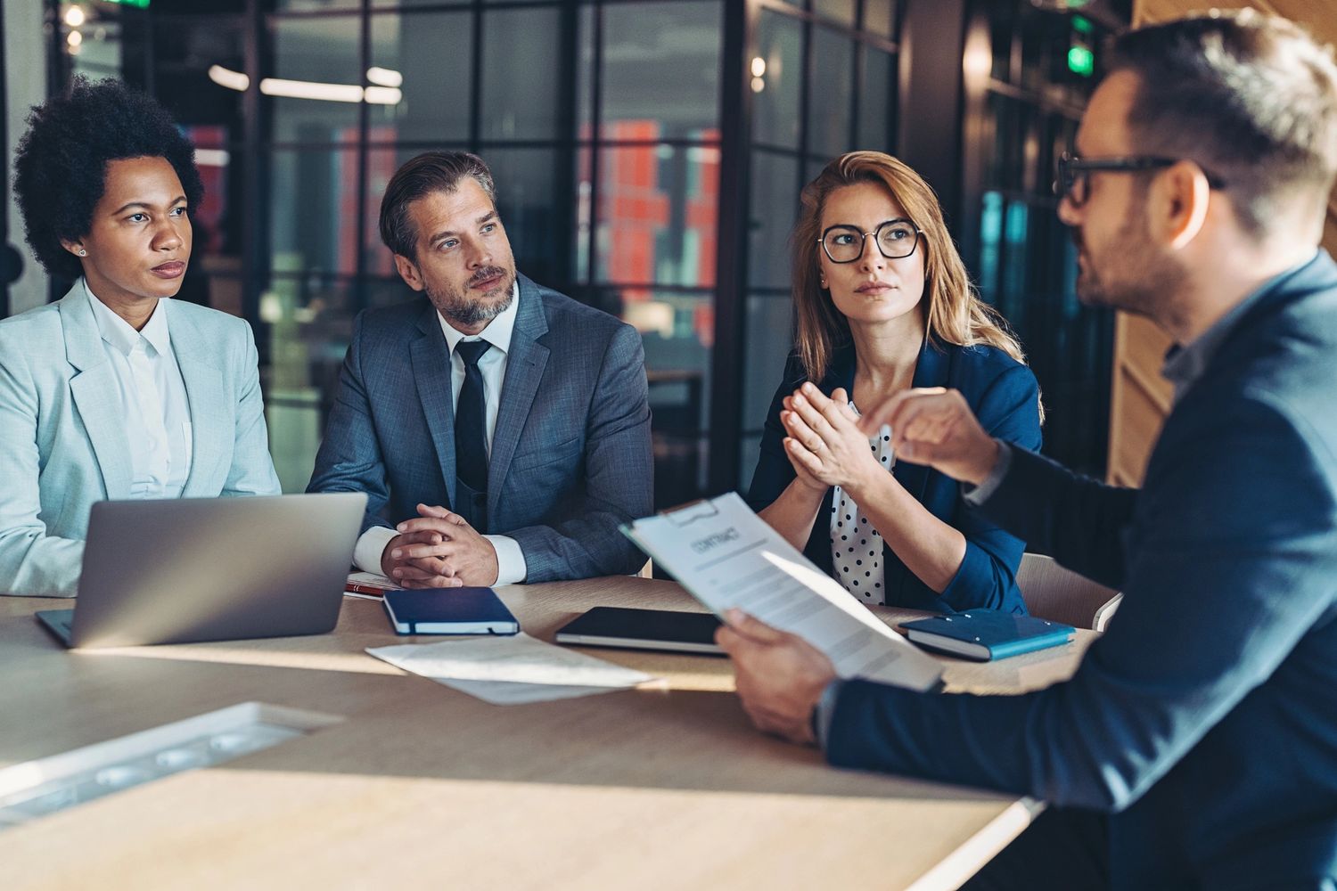 Four professionals engaged in a serious business meeting in a modern office.