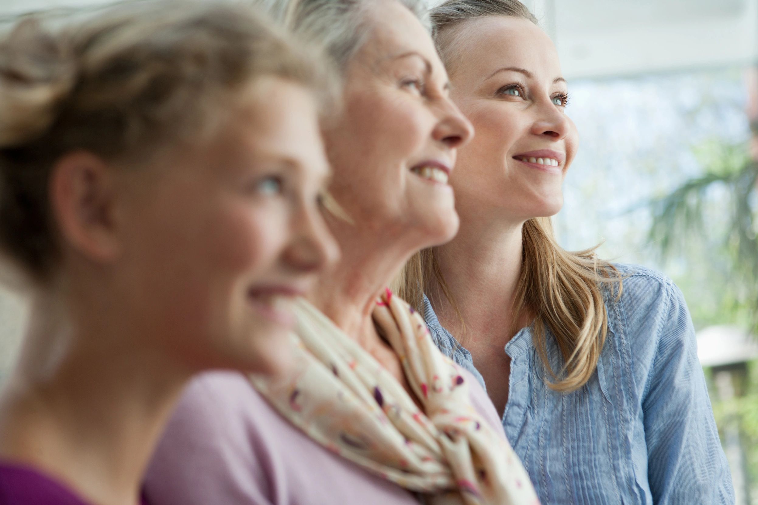 Three generations of women looking forward with smiles.