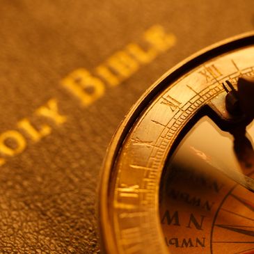 A close-up of a golden compass resting on a Holy Bible.