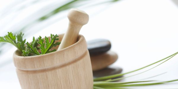 Wooden mortar and pestle with green leaves and stones for spa relaxation.