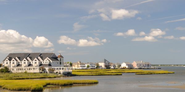 Coastal houses by a calm waterway under a blue sky with scattered clouds.