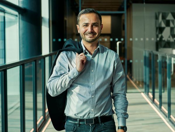 Man in blue shirt smiling and carrying jacket over shoulder.