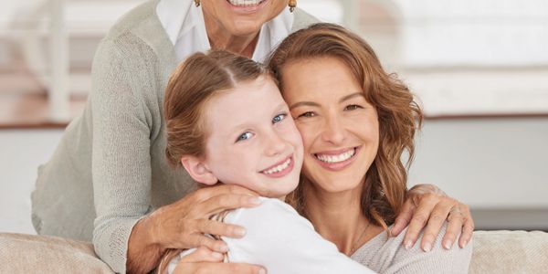 Three generations of women happily embracing each other on a couch.