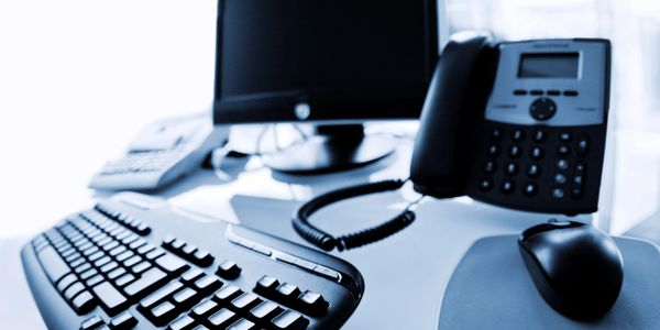 A modern office desk setup with a keyboard, mouse, phone, and monitor.