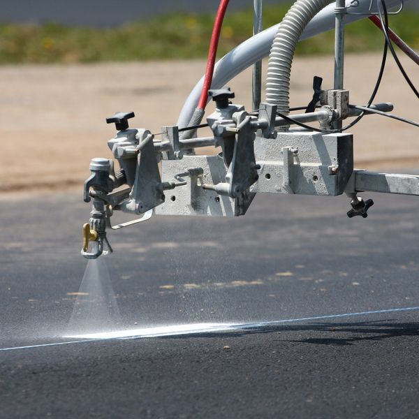 Machine spraying white paint to mark a line on asphalt.