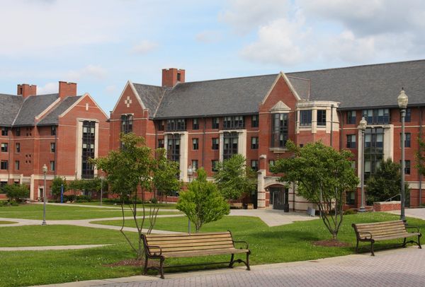 Red-brick university dormitory buildings with benches and trees in the foreground.