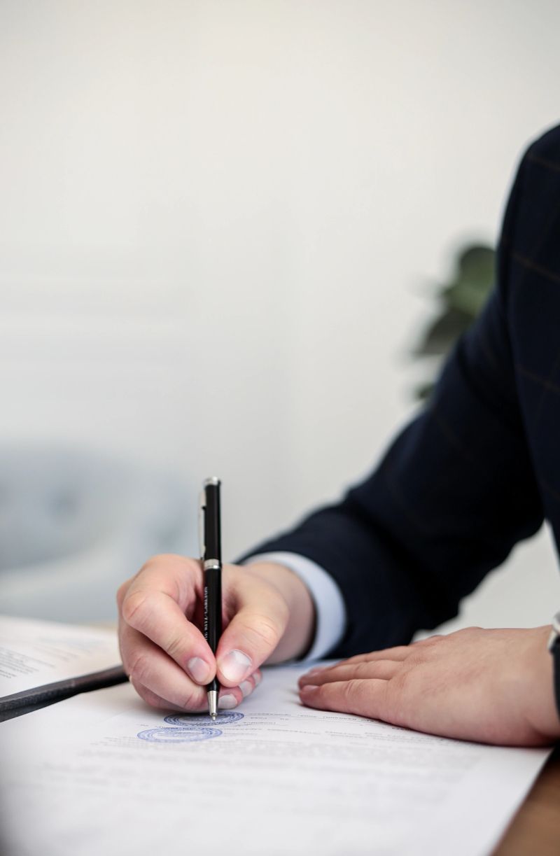 A man in a formal business suit is captured in the act of signing documents, portraying a professional transaction or agreement.