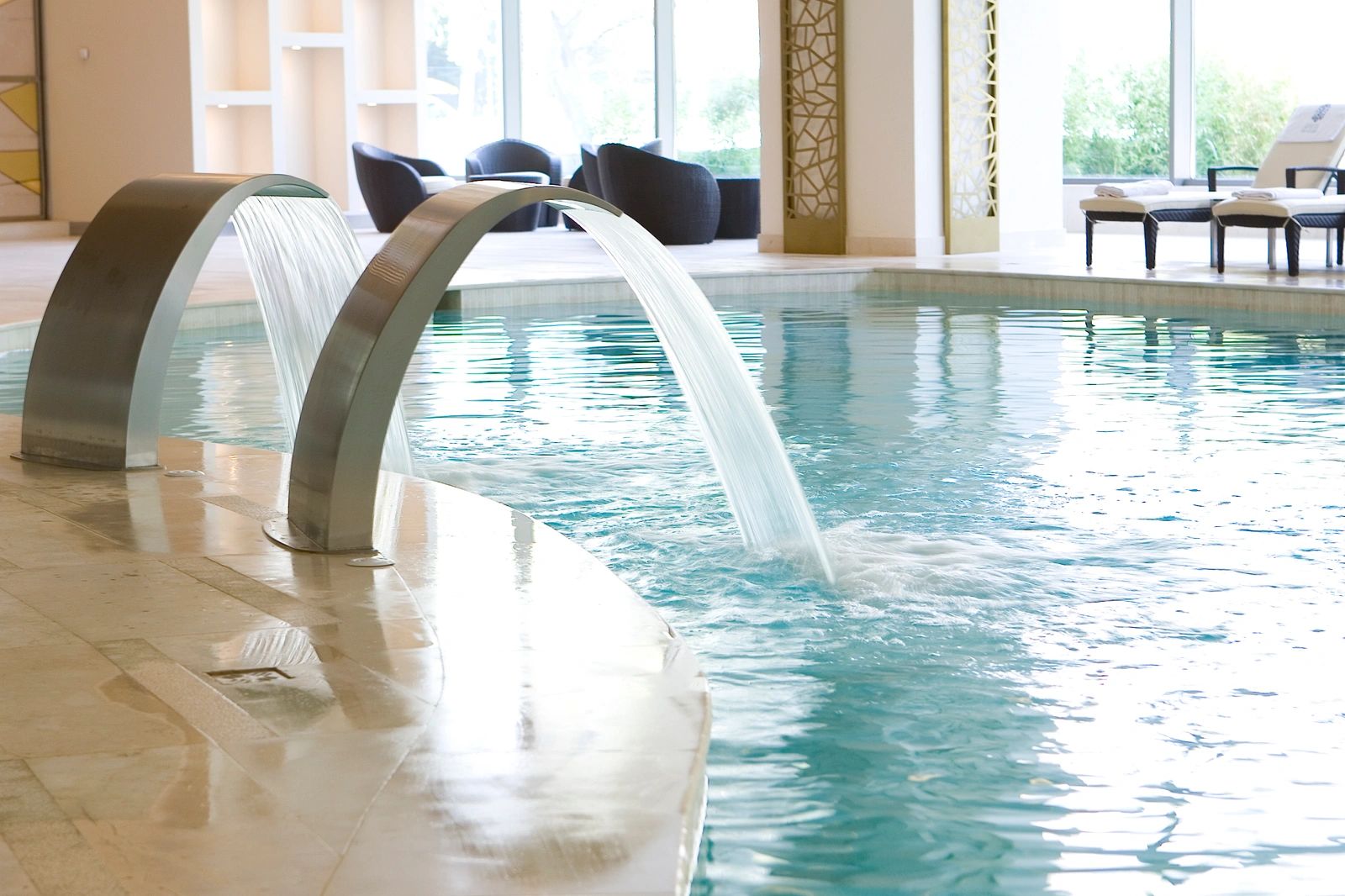 Modern indoor pool with water features and lounge chairs.