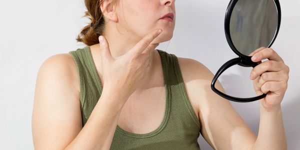 Woman examining her face in a handheld mirror.