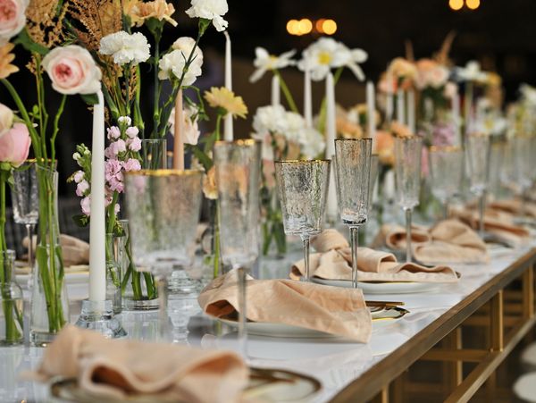 Elegant long table set with floral arrangements, candles, and glassware for a formal event.