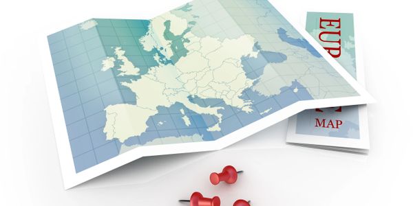 Folded map of Europe with three red push pins on a white surface.