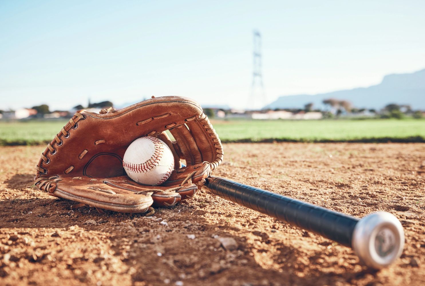 Baseball glove holding a ball next to a bat on a dirt field.
