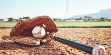Baseball glove, ball, and bat lying on a baseball field.