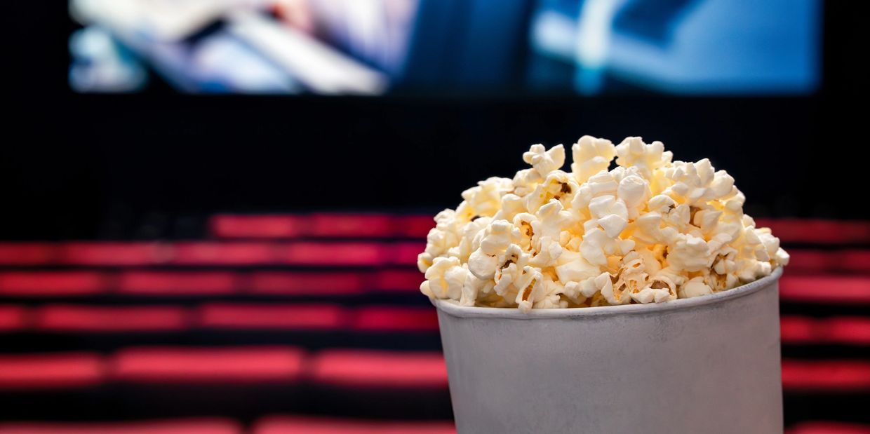 A bucket of popcorn in a movie theater with red seats and a blurred screen.