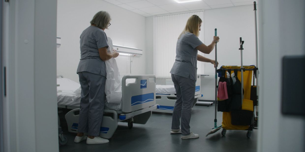 Two hospital workers cleaning and changing beds in a patient room.