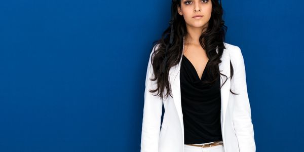 Confident woman in white suit stands against a blue wall.