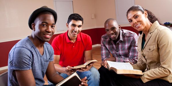 Group of four diverse adults reading books together.