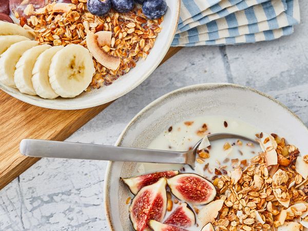 Two bowls of granola with milk and fresh fruit on a table.