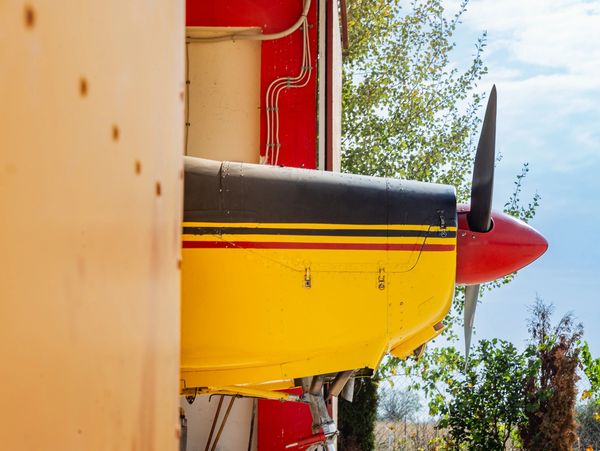 Close-up of a yellow and black airplane nose with a red propeller, parked at a hangar.