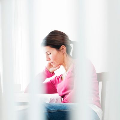 Woman in a pink sweater thoughtfully reading or working at a table.