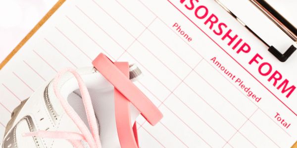 A white sneaker with a pink ribbon on a sponsorship form clipboard.