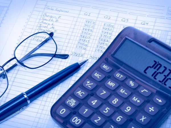 Calculator, glasses, pen on a financial expenses spreadsheet.