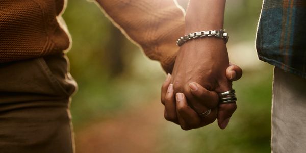 Two people holding hands with jewelry and rings in a warm outdoor setting.
