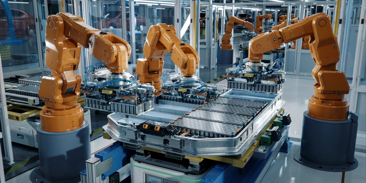 Robotic arms assembling battery cells in a high-tech factory.