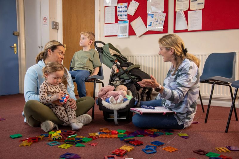 Full shot of a mother and her three children having a meeting with a childcare worker. They are in a community centre surrounded by toys. The institute is located in Seghill, Northumberland.