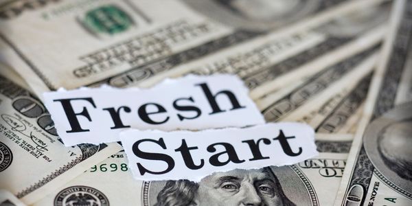 The phrase "Fresh Start" on torn paper over scattered US dollar bills.