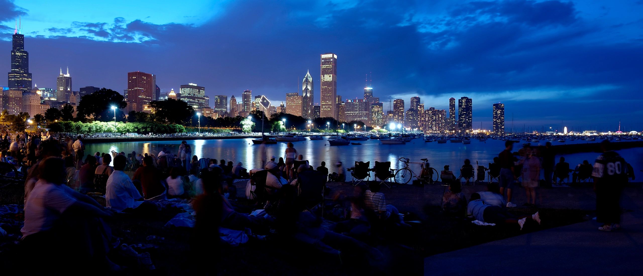 Crowd enjoying a serene evening by the city waterfront with illuminated skyline.