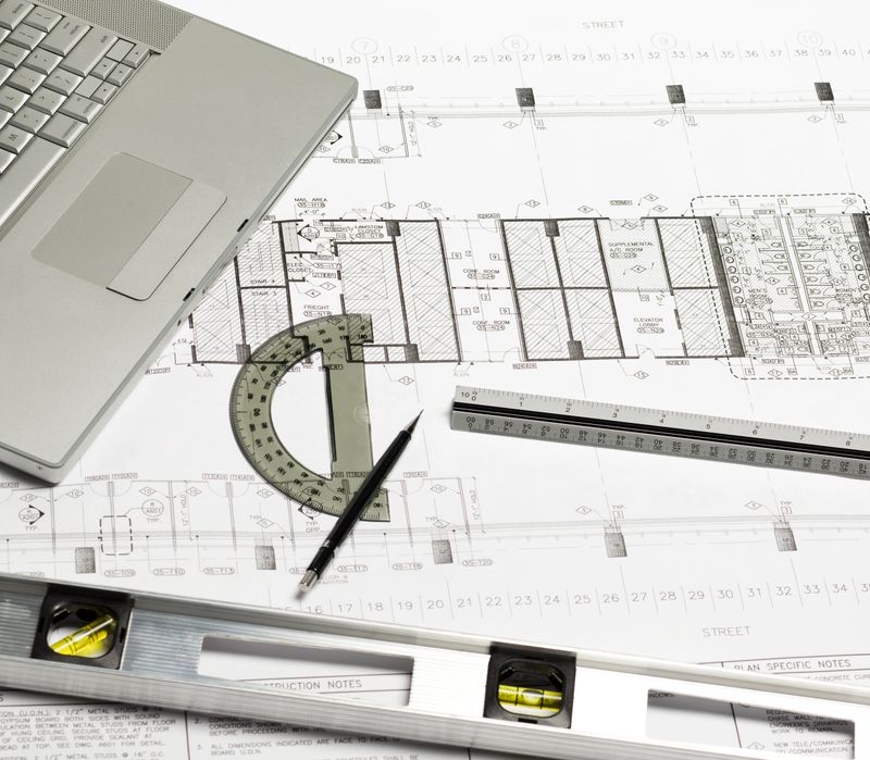 Architect's workspace with blueprints, laptop and drawing instruments.