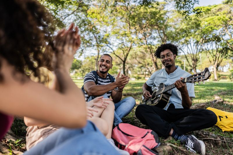 Student friends singing and playing guitar at university campus outdoors