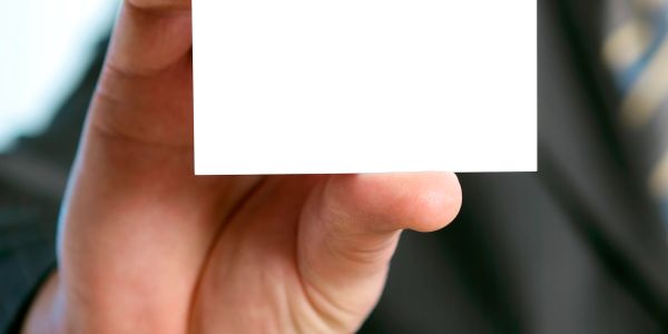 Hand holding a blank white card in focus, blurred background.