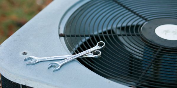 Two wrenches resting on an air conditioning unit's fan cover.
