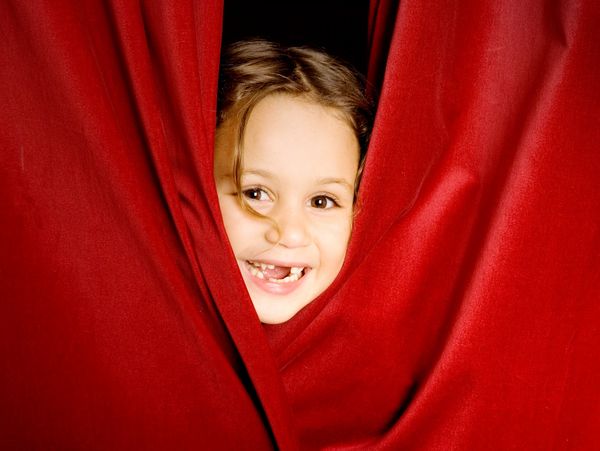 Happy child peeking through red curtains with missing teeth.