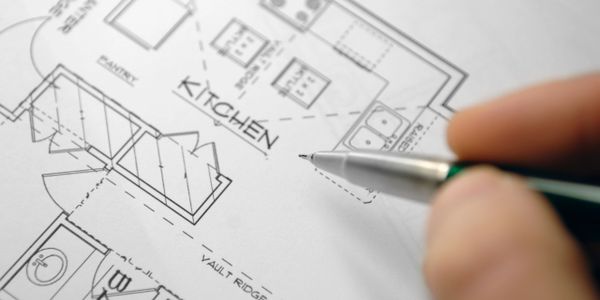 Close-up of hand holding pen over kitchen blueprint.