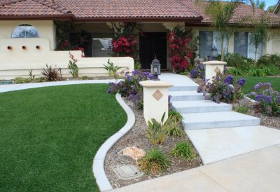 A house entrance with white steps, manicured lawn, and colorful flowers.