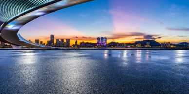 City skyline viewed from below a curved bridge at sunset.
