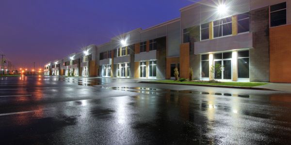 Empty industrial or commercial building complex at night with lights reflecting on wet pavement.