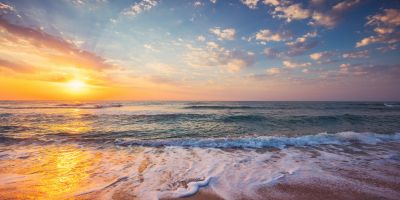 Sunset over a calm ocean with waves gently washing onto the sandy shore.
