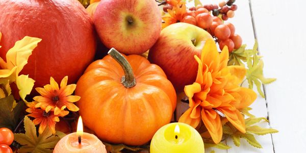 Autumn arrangement with pumpkins, apples, flowers, and candles on white wood.