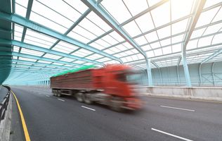 A red truck speeding through a covered highway tunnel with blue structural beams.