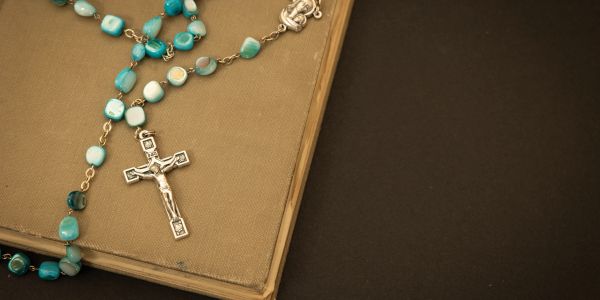 A turquoise rosary with a silver crucifix on a brown book.
