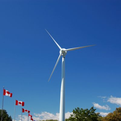 Wind turbine with Canadian flags under clear blue sky.