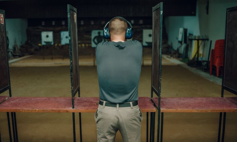 A professional man wearing earmuffs and goggles is practicing shooting a 9mm pistol inside a shooting range.
