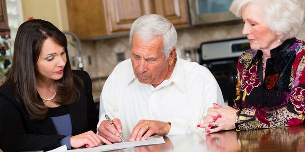 A woman helping an elderly couple sign documents at a table.